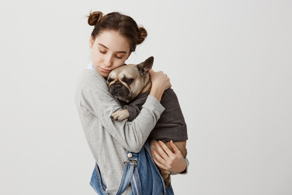 headshot of caucasian woman with closed eyes holding her lovely pet like child relaxing together. tender emotions of cute girl cuddling her small dog dressed in sweater. care, love concept